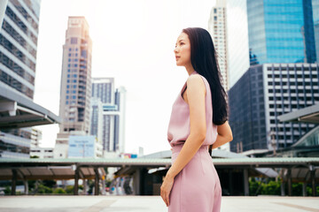 Businesswoman looking across towards city with tall modern buildings, head and shoulders of young adult woman business, achievement, goals, aspirations