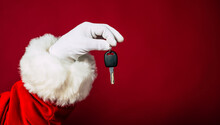 Close Up Photo Of Santa Claus Hand In White Glove Holds Key From New Apartment Or Auto Isolated On A Red Background