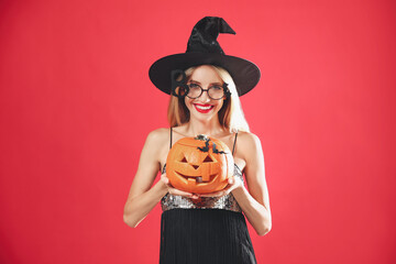 Poster - Beautiful woman in witch costume with jack o'lantern on red background. Halloween party