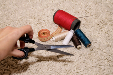 pools of different colors of thread, needle, meter lie on a white background, hand holds scissors