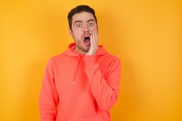 Wall Mural - Horizontal portrait of shocked Handsome man with sweatshirt over isolated yellow wall looks with great surprisment being very stunned, astonished with unexpected news, . Facial expressions concept.