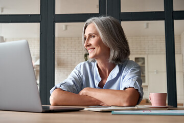 Wall Mural - smiling stylish mature middle aged woman sitting at home office workplace looking away. happy older 