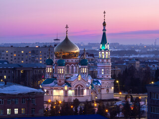 Assumption Cathedral in the center of Omsk from a height at sunset. Holy Assumption Cathedral and Cathedral Square from above. Pink-blue sky at sunset.