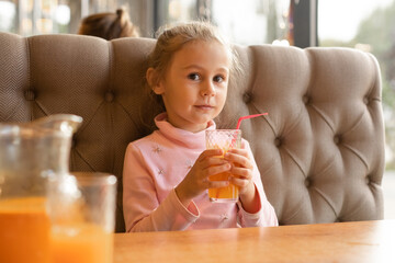 Cute little girl drinking sea buckthorn fruit drink in a cafe