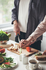 Close up photo of a caucasian couple slicing food in the kitchen preparing the meal together