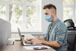 © kite_rin - Young businessman working in  office wearing medical protective face mask. Creative professional using laptop. Business, epidemic, pandemic, corona virus protection, healthy lifestyle, people concept
