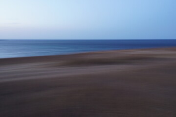 Abstract seascape of stormy blue water with waves, clear sky and dark sand