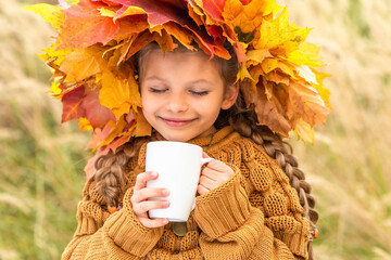 Wall Mural - A little girl with a wreath on her head drinks delicious tea in autumn.