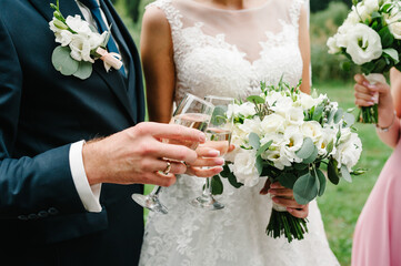 The bride and groom holds a glass of champagne and stand on nature at the wedding ceremony. Close up. Toast.