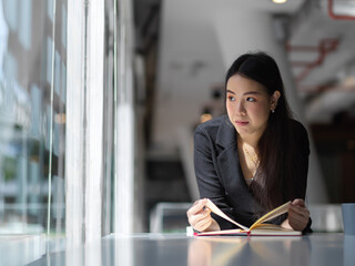 Businesswoman looking trough glass wall while reading her schedule book