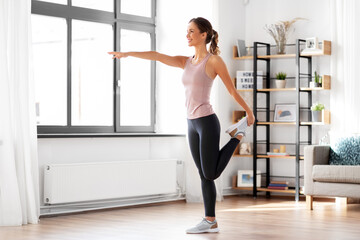 Wall Mural - sport, fitness and healthy lifestyle concept - smiling young woman stretching leg at home