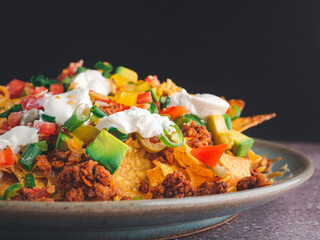 Side view of loaded minced pork nachos on plate with black wall background. Space for text. Concept of Mexican food