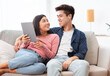 © Prostock-studio - Chinese Couple Using Tablet Watching Movie Sitting Of Sofa Indoor