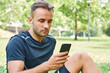 © Cavan Images - Man with his smart phone sitting on the grass in a park after training. Healthy and healthy life. Health and sport concept.