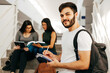 © kleberpicui - Portrait of young Brazilian student with backpack carrying books in college. Other students in the background.