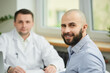 © Roman Tyukin - A bald male patient is smiling near a caucasian doctor in a white lab coat in a hospital. A happy man with a beard at an appointment in a doctor's office.