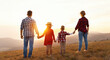 Happy family: mother, father, children son and daughter stand with their backs holding hands on  sunset.