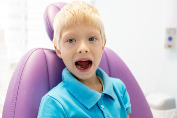 a child a five year old boy in a blue t shirt is sitting in a lilac chair in a white office