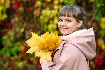 Cute smiling girl in autumn clothes holding a bouquet of autumn leaves.