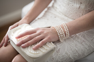 Wall Mural - A woman wearing a string of pearls as a bracelet a pearl covered purse dressed in a white lace dress lit by natural light from a nearby window casting shadows