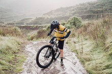 Full Body Of Female Cyclist On Muddy Mountain Path On Rainy Day