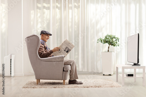 Fotomural Elderly man sitting in an armchair and reading a newspaper in a living room