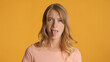 © Anton - Young sad woman sticking out tongue on camera over colorful back