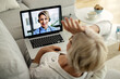 © Drazen - Close-up of mature woman having video call over laptop with her doctor.