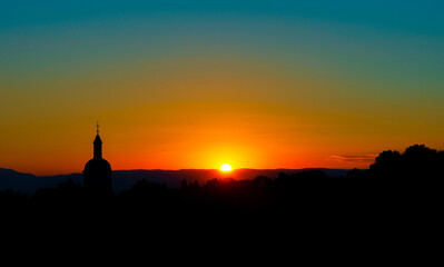 The stunning beauty and colors of the sunset overlooking the silhouettes of the Alps and the silhouette of a beautiful church