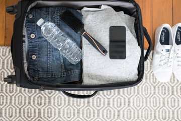 Small overnight weekender black suitcase packed clothes white shoes denim jacket grey jumper timber floor home casual travel trip explore traveller solo water bottle essentials looking down	