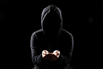 Dark shadowy hooded man in shadows with hands holding something