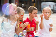 boy and his little girlfriends in elementary school age blowing bubbles outdoors.