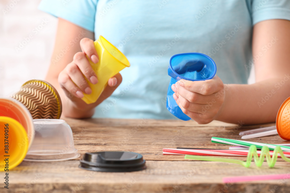 Woman crumpling plastic cups at table. Ecology concept
