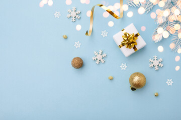 Christmas white gift with gold bow and ornaments on blue background, top view.