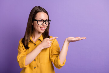 Poster - Photo portrait of smiling girl pointing at blank space holding on hand wearing glasses smiling isolated on vibrant purple color background