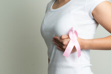 Pink Badge Ribbon On Woman Hand Touching Chest To Support Breast Cancer Cause. Breast Cancer Awareness Concept