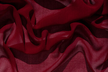 Smooth elegant burgundy chiffon fabric abstract background. Dark red wine silk satin luxury cloth texture on light surface for design. Luxurious Valentine's day backdrop. Wavy matte textured material