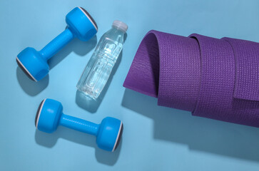 Rolled yoga mat, dumbbells and water bottle on a bright blue background. Healthy lifestyle concept. Top view Flat lay