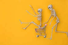 Shopping Trolley With Funny Skeletons On Yellow Background. Halloween Theme. Top View