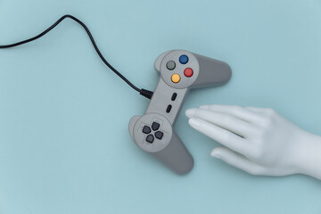 Wall Mural - Mannequin hand touching retro gamepad on blue background. Top view. Creative art, minimalism