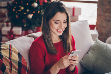 Wall Mural - Photo of positive girl typing letter on smartphone sit comfort couch in house indoors with x-mas christmas ornament