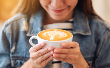 Closeup image of a beautiful young asian woman holding and drinking hot coffee in cafe