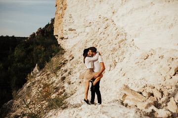 Wall Mural - Bearded man and stylish woman in hat hug and kiss each other while travelling in mountain.