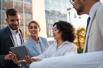 Wall Mural - Group of coworkers standing outside in front of office buildings discuss about business plan and looking at tablet.