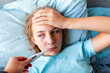© len44ik - Sick teenage little girl with high fever and headache laying in bed and holding thermometer in her mouth
