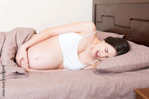 Fotografía Stressed pregnant woman lying in bed with her hand on her stomach, grimacing fro