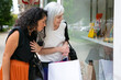 © Mangostar - Excited female friends holding shopping bags, standing at store outside, staring at accessories in shop window. Side view. Window shopping concept