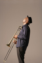 Side View Of A Happy African American Man With Trombone Standing Against Brown Background