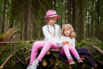 Two young girl playing and having fun together on walk in forest outdoors. Happy loving family with two sisters or female friends posing on nature landscape with with pine trees.