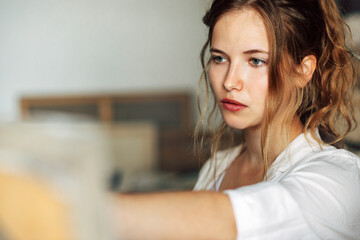 Wall Mural - Portrait of a female artist standing next the easel with canvas painting in the studio. Professional female painter draws in workshop.